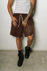 Bermuda estilo baggy de algodón color marrón oscuro, con cintura elástica y cordón blanco. Presenta un gran logo estampado en tono gris claro en la pierna derecha.