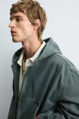 Cazadora negra de algodón con efecto lavado, corte relajado y capucha ajustable. Presenta cierre frontal de cremallera, bolsillos frontales tipo canguro y elásticos en puños y bajo.