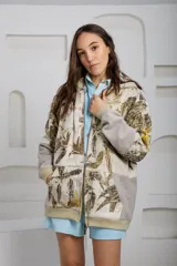 Canguro con capucha y cierre frontal, color beige con estampado de hojas en tonos marrones y amarillos. Mangas largas en color gris.