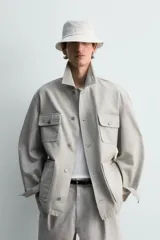 Cazadora de corte relajado confeccionada en tejido de algodón compacto con efecto lavado. Presenta cuello de solapa, manga larga con puños abotonados y cierre frontal de botones. Incluye cuatro bolsillos frontales: dos de plastrón con solapa en el pecho y dos bolsillos dobles de plastrón en la cadera.