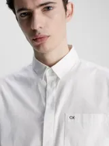 Camisa blanca de popelín de algodón superelástico, corte boxy, cuello en punta, manga corta, bolsillo de parche en el pecho, bajo recto y logo monograma de Calvin Klein estampado en el pecho.