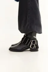 Bota de caña baja confeccionada en cuero con textura crocco, color bordó. Presenta taco cuadrado, punta cuadrada y un accesorio desmontable con doble hebilla metálica y tachas decorativas.