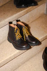 Bota tipo borcego de cuero en tono marrón con efecto desgastado, cordones bicolores en amarillo y naranja, y suela de goma dentada con costura blanca visible.