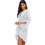 Vestido de playa corto en tejido calado color crema, con mangas largas acampanadas y diseño asimétrico con volado en el ruedo. Presenta un escote redondo con abertura frontal y cordón ajustable.