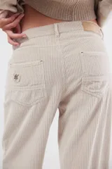 Pantalón de pana de corte ancho y tiro medio-bajo, con diseño de cinco bolsillos y acabado lavado. Presenta un aplique cuadrado decorativo en una de las piernas y un pin bordado de la marca.