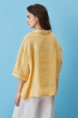 Camisa blanca de lino, con mangas anchas a tres cuartos, cuello clásico, cierre frontal con botones y detalles de calados verticales en la parte central y en los puños.