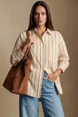 Camisa de corte oversize con estampado de rayas verticales en tonos beige y mostaza. Presenta cuello clásico, cierre frontal con botones, bolsillo aplicado en el pecho y mangas largas con puños abotonados.