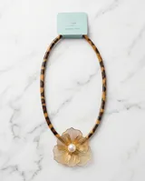 Collar con cordón de efecto carey animal print y dije central de acero bañado en oro con diseño de flor calada y perla en el centro.