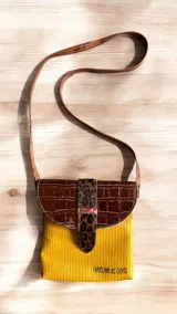 Bandolera de cuero natural de diseño compacto, marca Carolina De Cunto, línea Ottenta. Combina cuerpo amarillo mostaza con textura, solapa marrón con textura símil cocodrilo, tira central de animal print y correa fina larga ajustable. Cuenta con solapa con broche imán, forro interior con tela estampada y bolsillo interno con cierre.