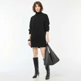 Vestido tipo sweater de punto color negro, con cuello alto y detalle de botones decorativos en el hombro. Presenta mangas largas con puños ajustados y un corte recto.