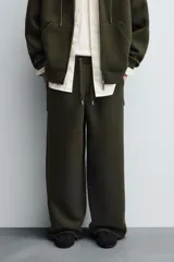 Pantalón de corte wide fit confeccionado en tejido técnico con efecto neopreno. Presenta cintura elástica ajustable con cordón, perneras anchas con costura frontal, bolsillos laterales y bolsillos traseros de plastrón.