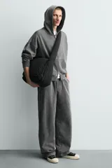 Bolso de hombro confeccionado en tejido técnico acolchado de color negro. Presenta un diseño de solapa con cierre magnético y cremallera, asa de hombro integrada y compartimentos interiores.