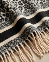 Poncho abierto con estampado animal print tipo leopardo en tonos grises y negros, con bandas horizontales en los bordes y flecos colgantes en el ruedo.