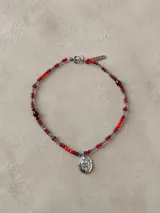 Gargantilla de cuentas de cristal en tonos rojos y grises, con dije central de escudo metálico plateado y cierre de mosquetón.