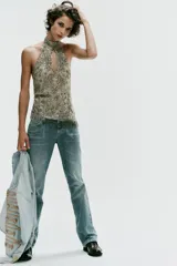 Top halter confeccionado en mezcla de poliamida, color verde militar, con diseño cut-out en el escote, espalda descubierta y aplicaciones de abalorios y lentejuelas brillantes. Presenta bajo recto con flecos colgantes de cuentas y cierre posterior con botones en el cuello.
