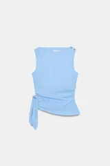 Top celeste de popelina sin mangas, con cuello barco y botones dorados en el hombro. Presenta diseño fruncido en los laterales y detalle de nudo con tiras en la cintura.