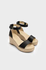 Sandalias de tacón en cuña forrada en yute trenzado, con capellada de cuero negro, tira en el talón y tira ajustable al tobillo con hebilla metálica.