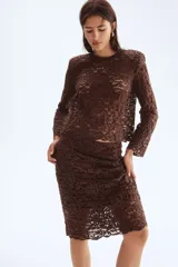 Pollera ajustada color marrón oscuro, confeccionada en encaje floral con bajo festoneado. Es de tiro alto y tiene un forro corto interior.