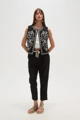 Chaleco negro sin mangas, de corte corto y abierto, con bordado floral en hilo blanco que recorre el borde del cuello y los frentes.