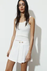 Falda pantalón de tiro bajo con diseño de pliegues en el delantero y cierre frontal con botones metálicos decorativos.