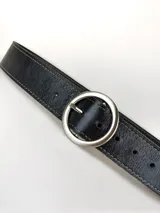 Cinto de cuero negro con textura granulada, costuras decorativas en los bordes y hebilla circular metálica en acabado plateado mate.