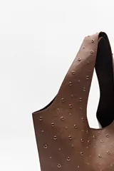 Bolso tipo tote negro de cuero sintético con micro tachas metálicas plateadas. Tiene asas integradas para llevar al hombro.