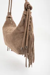 Cartera tipo bandolera de gamuza sintética color bordó, con diseño de flecos largos en la parte inferior y correa ajustable con nudo lateral. Incluye cierre superior y detalle de placa metálica con logo.