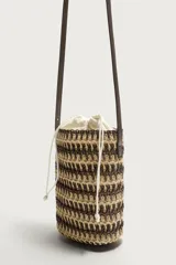 Bandolera vertical con acabado trenzado en tonos tostados y oscuros, cuenta con bolsa interior de tela con cierre de cordón ajustable y correa fina para el hombro.