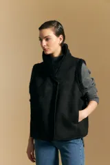 Chaleco negro de gamuza sintética con interior y bordes de corderito sintético. Presenta un diseño sin mangas con cuello solapa y cierre frontal.