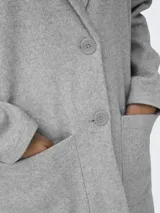 Blazer largo de corte recto y estilo minimalista, confeccionado en tejido de punto gris melange. Presenta cuello con solapas, cierre frontal de dos botones y dos bolsillos frontales de parche.
