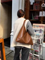 Cartera slouchy marrón de cuero sintético con detalles de tachas metálicas en las costuras y correa de hombro integrada.