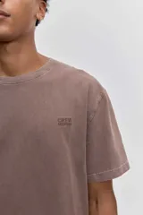 Remera de algodón color marrón con efecto lavado, de corte clásico y cuello redondo. Presenta un pequeño bordado de un pájaro en el pecho.