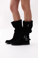 Bota de caña alta color marrón chocolate, confeccionada en gamuza. Presenta dos correas desmontables con hebillas metálicas plateadas.