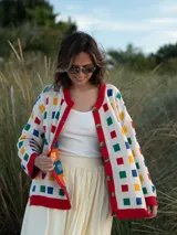 Cárdigan de punto color crudo con botones y ribete rojo. Presenta un patrón de cuadrados de colores (azul, rojo, amarillo y verde).