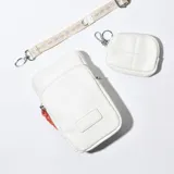 Porta celular blanco de cuero sintético con correa de tela estampada y monedero redondo con cierre y gancho mosquetón.