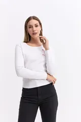 Remera de manga larga en color blanco, confeccionada en algodón con textura acanalada. Presenta un cuello redondo y una pequeña estampa minimalista en color rojo en la parte superior del pecho.