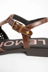 Sandalias de cuero marrón, con puntera cerrada de diseño trenzado, empeine liso y tira ajustable con hebilla en el talón. Cuenta con suela plana y baja.
