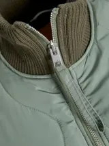 Campera acolchada de color gris oscuro, con diseño matelaseado de ondas, cuello alto en rib, cierre frontal con cremallera metálica y bolsillos frontales aplicados.