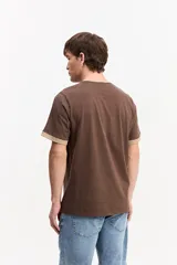 Remera marrón de manga corta confeccionada en algodón, con cuello redondo y ribetes en contraste de color tostado en el cuello y los puños. Presenta estampa frontal con la frase "your vibe attracts your tribe" y el logo de Mistral.