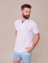 Remera polo blanca de manga corta, con detalles en azul marino en el cuello y los puños, y el logo bordado en el pecho.