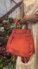 Cartera mochila de diseño versátil, color rosado, confeccionada en material sintético impermeable. Cuenta con doble asa superior, correas ajustables para usar como mochila, compartimento principal con cierre y bolsillo frontal con cierre decorado con tirador largo.