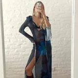 Vestido largo de microtul translúcido con estampado floral en tonos azules y negros, manga larga y abertura lateral.