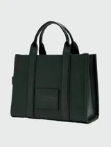 Bolso tipo tote de cuero negro, modelo The Leather Medium Tote Bag de Marc Jacobs. Presenta doble asa superior, correa ajustable para el hombro y el texto grabado "THE TOTE BAG MARC JACOBS" en el frente.