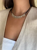 Collar corto de cuero negro con cuentas plateadas y dijes circulares colgantes.