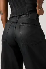 Pantalón de jean con acabado encerado negro, de corte super baggy y silueta tipo barril, con diseño de cinco bolsillos y cierre frontal con botón y cremallera.