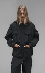 Chaqueta técnica liviana de microfibra con acabado mate, diseño con mangas desmontables que permiten convertirla en chaleco. Cuenta con cuello tipo camisa, cierre frontal oculto, cuatro bolsillos frontales de gran tamaño y puños elásticos. Incluye logo bordado en relieve en el pecho.