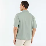Camisa de manga corta color verde claro, de corte holgado, con cuello solapa y bolsillo parche en el pecho.