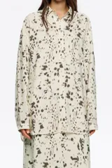 Camisa de corte recto con cuello camisero, mangas largas y puños abotonados. Presenta un estampado abstracto en tonos marrón oscuro sobre fondo crema.