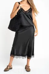 Falda midi negra de acabado satinado, corte al bies, con detalle de encaje en el ruedo.