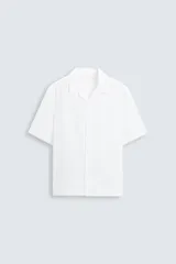 Camisa blanca de lino con corte relajado, cuello bowling y manga corta. Presenta cierre frontal de botonadura y bajo con aberturas laterales.
